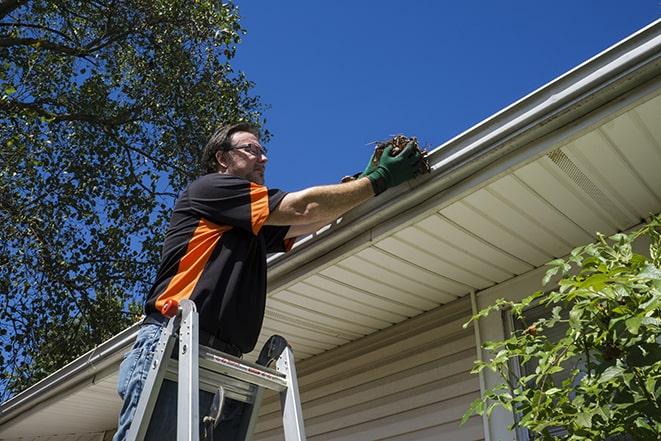 smiling worker fixing gutters on a residential home in Alexander